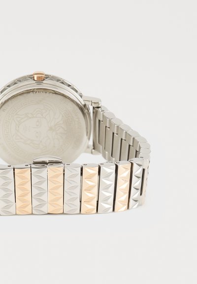 Roostevabast terasest kell, millel on kahe tooniga link-randmete ahel ja mustriline disain. Ümmargune hõbedane kest, millel on ringikujuline graveeritud tagakülg ning kuldne aksent.