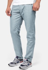 Lyseblå, slim-fit bukser laget av et glatt stoff, med sidelommer og rette ben, sammen med grå og marineblå joggesko.