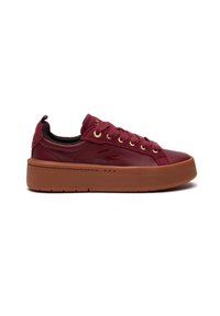 Sneaker in pelle bordeaux con tomaia testurizzata, occhielli dorati e suola in gomma marrone spessa. Presenta un'etichetta sul tallone e dettagli di cucitura.