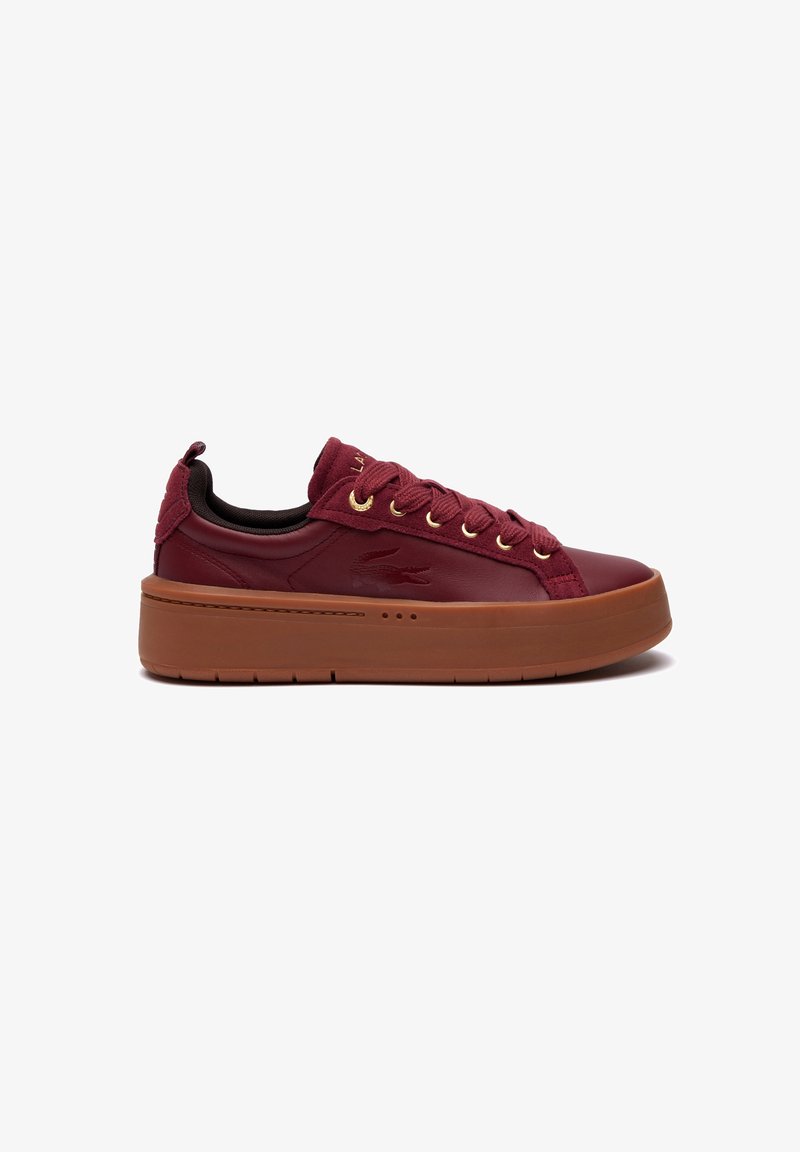 Sneaker in pelle bordeaux con tomaia testurizzata, occhielli dorati e suola in gomma marrone spessa. Presenta un'etichetta sul tallone e dettagli di cucitura.