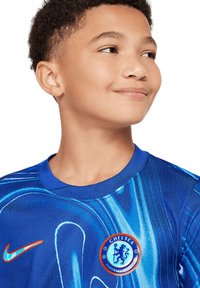 Chelsea jalkapallopaita, jossa on sininen muotoilu abstrakteilla kuvioilla, pyöreä joukkueen emblem ja oranssi Nike-logo.