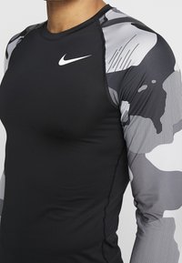 Czarna koszulka sportowa z długim rękawem, z szarym i białym wzorem w kamuflaż na rękawach, oraz małym białym logo na klatce piersiowej.
