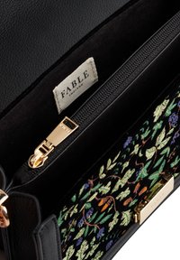 Black leather handbag with a colorful floral embroidery on a dark background. Features a gold zipper and a fabric label reading "FABLE."