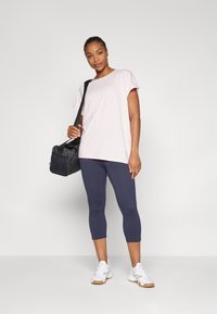 Light pink short-sleeve athletic shirt, paired with dark blue capri leggings and white athletic shoes. Black bag with shoulder strap.