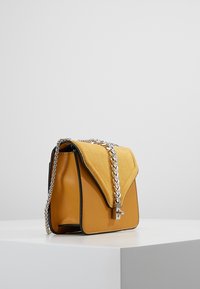 Borsa gialla con tappo in suede e corpo in pelle, dotata di tracolla e chiusura in catena argentata, forma rettangolare e accenti neri a contrasto.