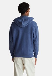 Blauwe fleece hoodie met een contrasterende capuchon, textuurstof en elleboogpatches. Beschikt over een losse pasvorm en ribbels aan de mouwuiteinden.