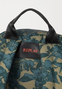 Sac à imprimé floral vert avec des accents noirs, doté d'une poignées robuste et d'un label rouge "REPLAY" bien visible sur une surface texturée.