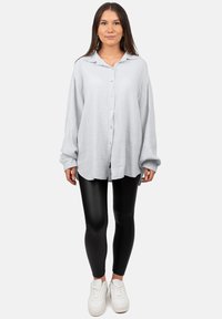 Camicetta grigia chiara con un design a pieghe testurizzato, abbinata a leggings neri e sneakers bianche. Le maniche lunghe sono leggermente oversize.
