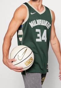 Maglia da basket verde con "MILWAUKEE" e numero "34" in bianco. Logo Nike sul petto, tessuto leggero, abbinata a una palla da basket bianca.