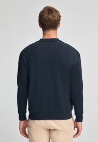 Mörkblå sweatshirt med långa ärmar, rund halsringning och ribbade mudd. Slät textur, klassisk design, inga synliga logotyper eller mönster.