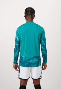 Türkisfarbenes Sportshirt mit langen Ärmeln und abstrakten blauen Mustern auf den Ärmeln, glattem Stoff, Rundhalsausschnitt und einem einfarbigen Rücken.