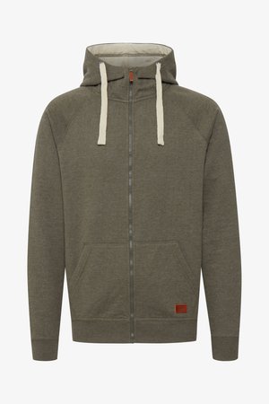 Olive roheline tõmblukuga kapuutsiga pumpphüüd, mis on valmistatud pehmest kangast, kuhu kuuluvad voodriga kapuuts, beežid paelad, taskud ja väike brändi naha etikett.