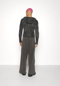 Dunkelgrauer gestrickter Hoodie mit geripptem Muster und längerem Rücken, kombiniert mit weiten, schiefergrauen Hosen aus weichem Stoff. Minimalistisches Design.