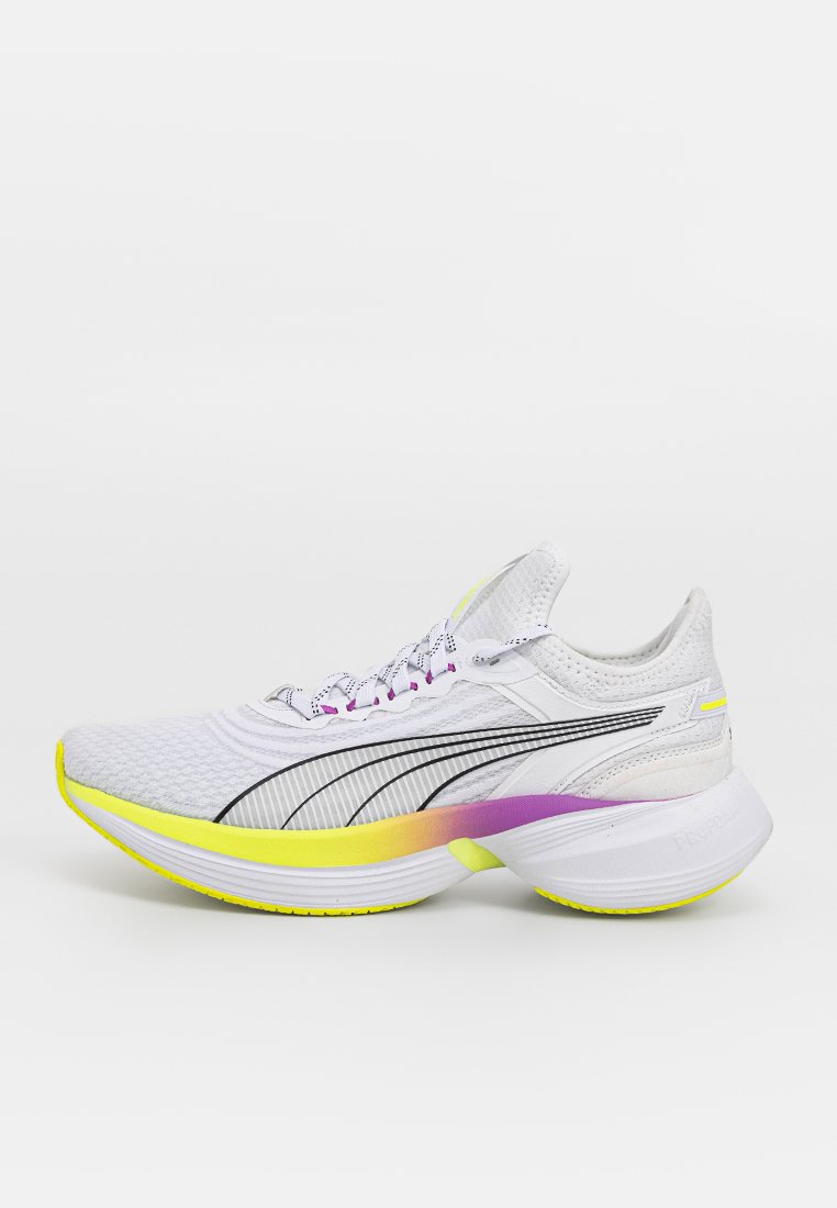 Zapatilla de running blanca con parte superior de malla, rayas negras y suela en contraste amarilla y morada. Cuenta con un collar acolchado y diseño de cordones.