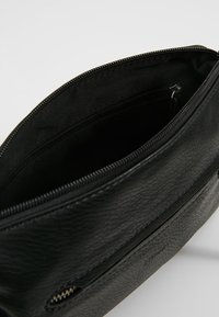 Borsa in pelle nera con una finitura tessurizzata, dotata di chiusura con zip e una tasca interna con zip. L'interno è foderato in tessuto.