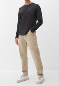 Camisa negra de manga larga y cuello redondo combinada con pantalones beiges y zapatillas beiges. Ajuste casual, textura suave, diseño simple y sin estampados.