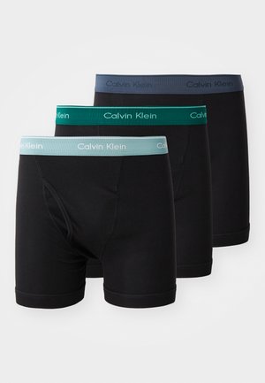 Tres pares de bóxers negros con cinturillas elásticas en gris, azul verdoso y verde, que presentan el logo de "Calvin Klein" en colores contrastantes.