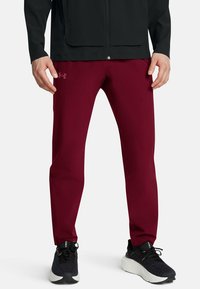 Pantalones deportivos burdeos de corte slim, con textura suave y detalle del logo. Combinados con zapatillas negras texturizadas y una chaqueta negra.
