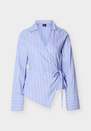 Ανοιχτό μπλε πουκάμισο τύπου wrap με κάθετες λευκές ρίγες, μακριά μανίκια και κλείσιμο με δέσιμο στη μέση. Διαθέτει μυτερό γιακά και ασύμμετρη τελική γραμμή.