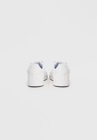 White sneakers with a smooth leather finish, rounded toe, low profile, and subtle stitching details. Black sole provides traction.