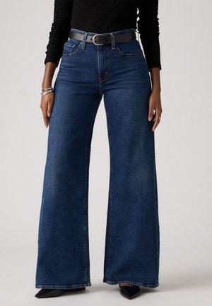 Pantalones vaqueros de mezclilla oscuros de pierna ancha con una cintura alta, que cuentan con cinco bolsillos y un cinturón negro. Textura suave, detalle de costura en contraste.