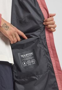 Zwarte Texapore Ecosphere Pro jas aan de binnenkant met een roze rand; beschikt over een zak en een label met details over waterdichte en ademende technologie.