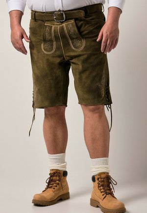 Hombre con pantalones cortos de lederhosen de ante marrón con bordado, calcetines blancos gruesos, botas marrón claro con cordones y una camisa blanca de manga larga.