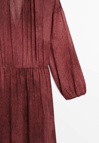 Robe longue bordeaux à manches longues avec une taille cintrée, fabriquée dans un tissu transparent et texturé, avec des détails froncés et des manches ballon.