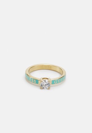 Bague anneau en or avec des sections en émail turquoise portant le mot « GUESS » et une pierre précieuse ronde claire unique dans un sertissage à quatre griffes.