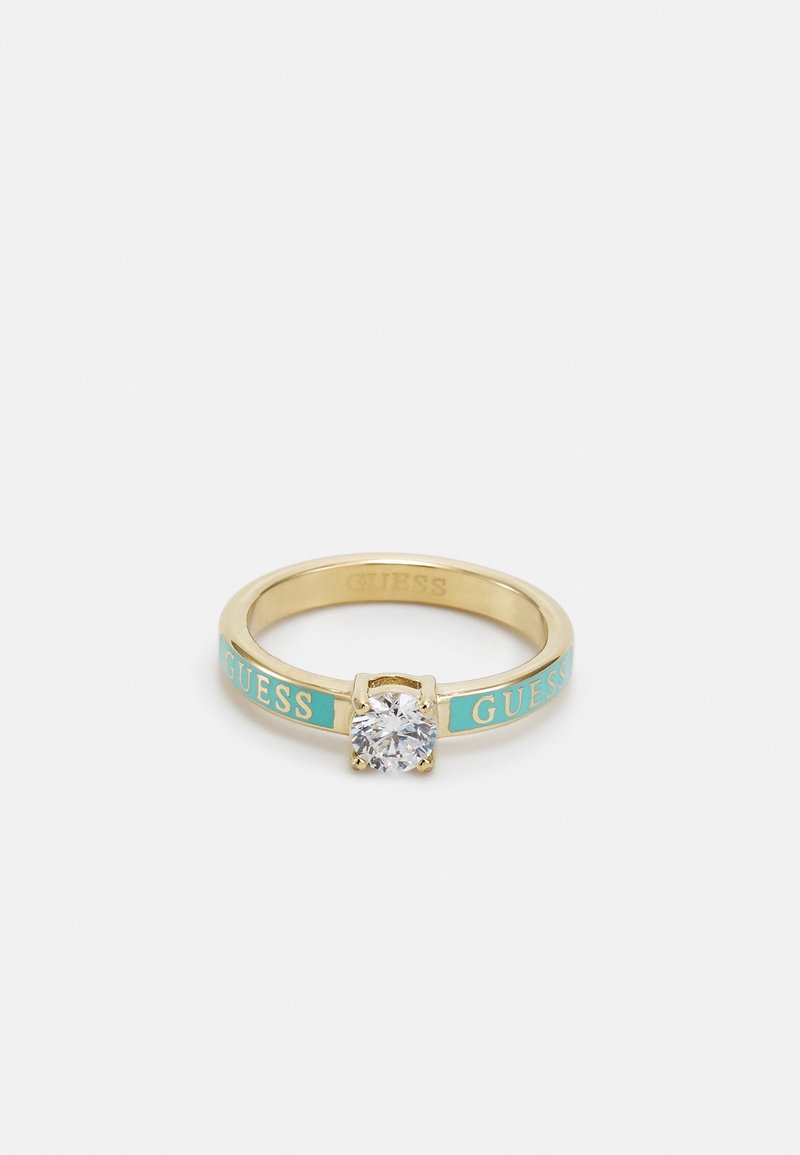 Bague anneau en or avec des sections en émail turquoise portant le mot « GUESS » et une pierre précieuse ronde claire unique dans un sertissage à quatre griffes.