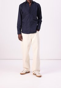 Navy long-sleeve shirt with a button-down collar, paired with beige wide-leg pants and white sneakers featuring black stripes on the side.
