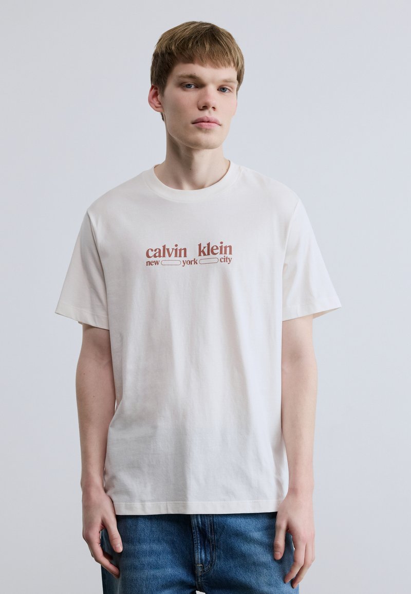 Λευκό βαμβακερό t-shirt με στρογγυλή λαιμόκοψη και κοντά μανίκια, με το κείμενο «calvin klein new york city» σε σκουριά απόχρωση στο κέντρο.