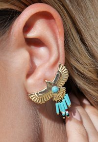 Des boucles d'oreilles en forme d'aigle doré ornées d'une pierre turquoise et de pendentifs en turquoise et perles multicolores. Design texturé avec plusieurs couches.
