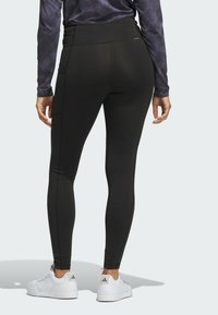 Zwarte leggings met een hoge taille, voorzien van zijzakken en minimale naadafwerking. Gepaard met witte sneakers.
