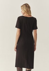 Vestido midi negro con mangas cortas y escote redondeado. Presenta un discreto cierre en la parte posterior y una tela suave y opaca. Diseño simple y ajustado.