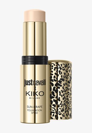 Bâton de fond de teint doré avec embout beige, texte noir « Just Cavalli x Kiko Milano », et bouchon imprimé léopard à côté.