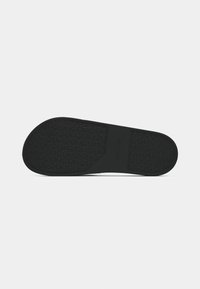 Semelle de chaussure noire avec grip à motif et une partie centrale lisse affichant un petit nom de marque embossé.