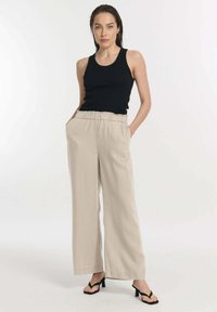 Zwarte mouwloze top, gecombineerd met lichtbeige wijde broek met elastische tailleband, zakken en een losse, vloeiende pasvorm.