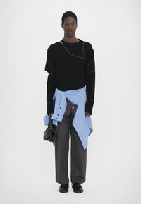 Black oversized sweater with gray stitching, light blue shirt tied around waist, gray wide-leg pants, black shoes, and small black handbag.