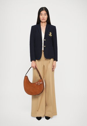 Marinblå blazer med guldemblem och knappar, vit topp, beige vida byxor och en brun mockaväska med en böjd silhuett. Svarta skor.