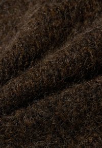 Tissu brun texturé avec une apparence douce et duveteuse. Le matériau est tissé avec des nuances variées de fibres brunes, créant de la profondeur et de la chaleur.