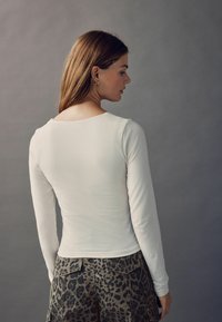 Langærmet hvid bluse med rund halsudskæring, parret med leopardmønstrede shorts. Stofudtrykket virker glat og tætsiddende.