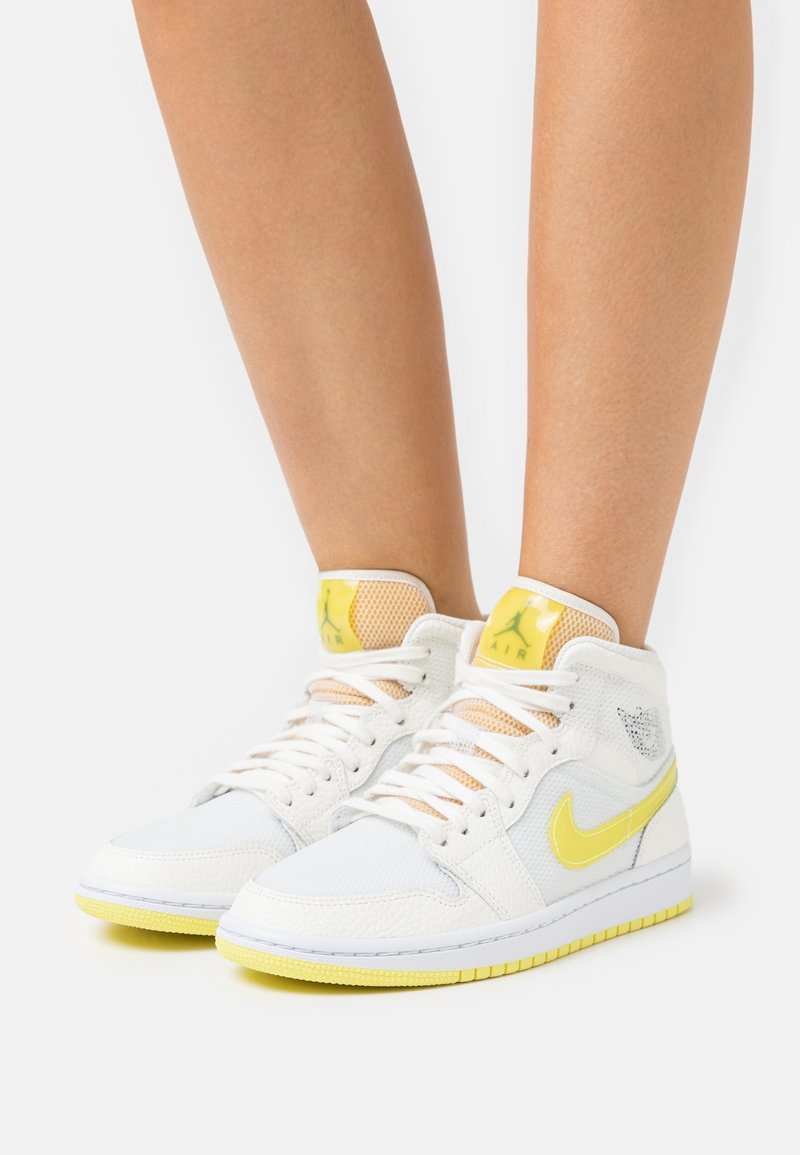 Person wearing white and yellow high-top Nike sneakers with laces, standing against a plain white background.