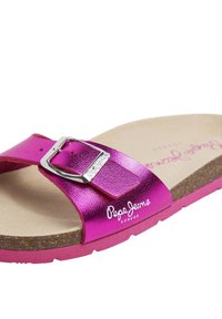 Rosa metallisk slidesandal med en silverfärgad spänne och korkfotbädd. Har en tryckt logotyp på fotbädden och ett strukturerat rem.