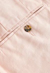 Tissu rose avec un bouton écaille cousu près d'une poche fendue fermée avec des coutures détaillées.