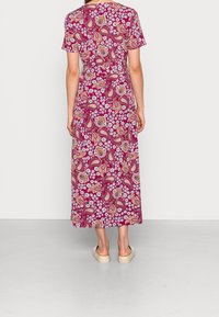 Maxi šaty v burgundské barvě s paisley a květinovým vzorem. Krátké rukávy, volný střih a viditelný elastický pás. Nosené s lehkými sandály.