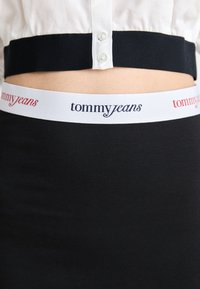 Juodas audinys apačioje su baltu elastingu liemeniu, ant kurio užrašyta "tommyjeans" mėlynos ir raudonos spalvos rašmenimis. Lygus paviršius ir prigludęs dizainas.