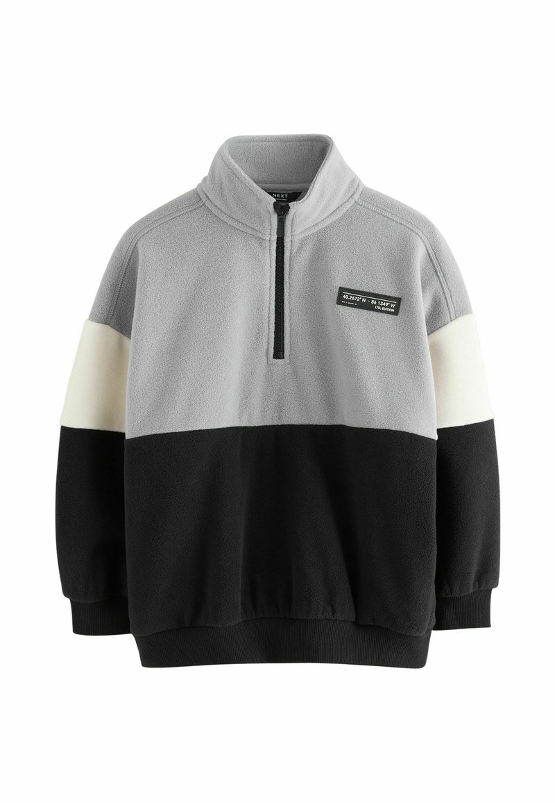 Fleece pullover med høj krave, der har grå, cremefarvet og sort farveblokke, halv lynlås foran og et mærke syet på brystet.