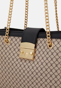 Beżowa torba na ramię z geometrycznym wzorem, czarnym skórzanym paskiem i złotym zapięciem. Posiada teksturowaną powierzchnię i łańcuszkowy uchwyt.