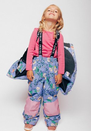 Pantaloni da neve blu con un motivo floreale colorato e dettagli rosa, dotati di bretelle nere regolabili. Il bambino tiene un cappotto nero con un motivo.
